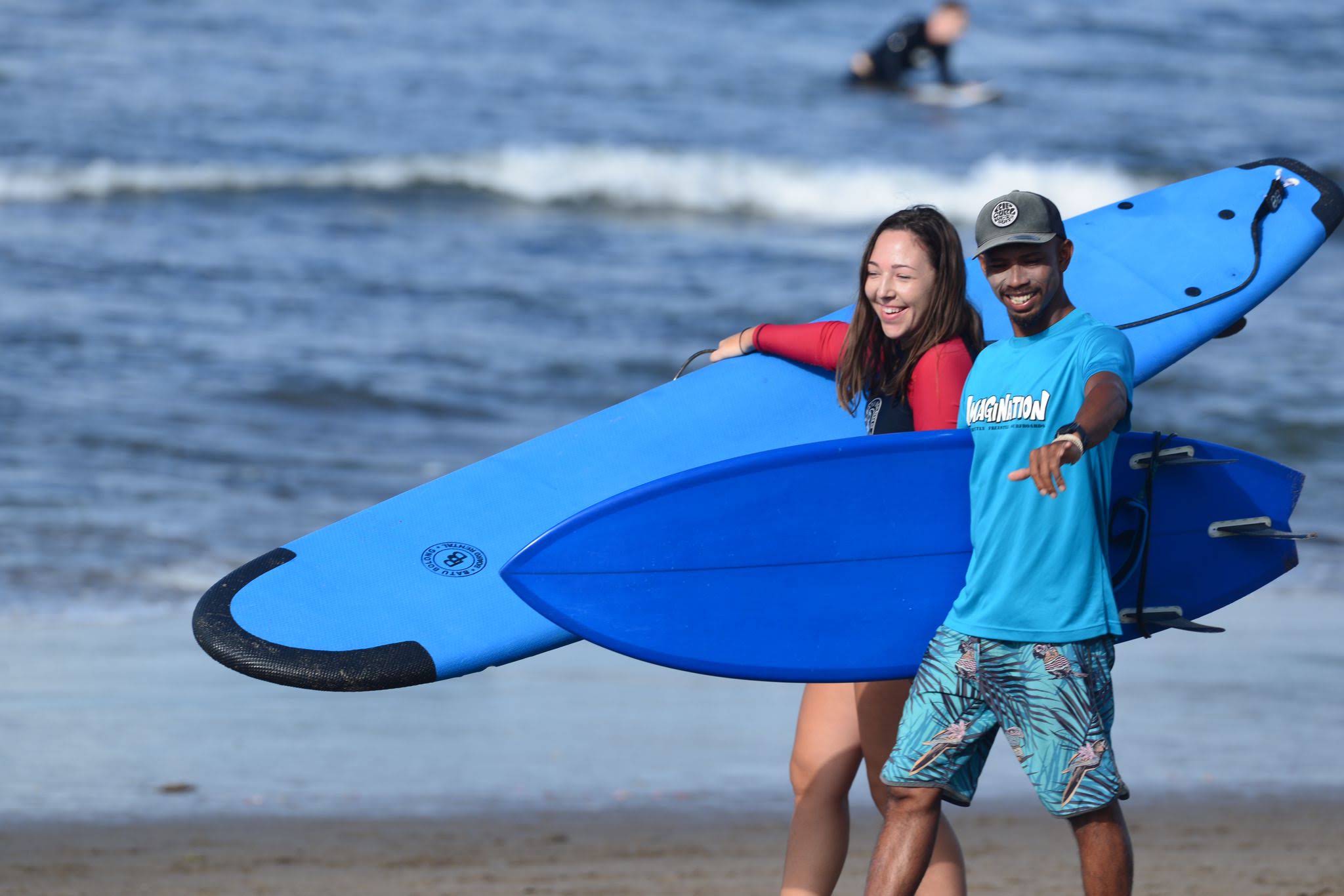 Agus walking with a surf student and boards on the beach in Canggu